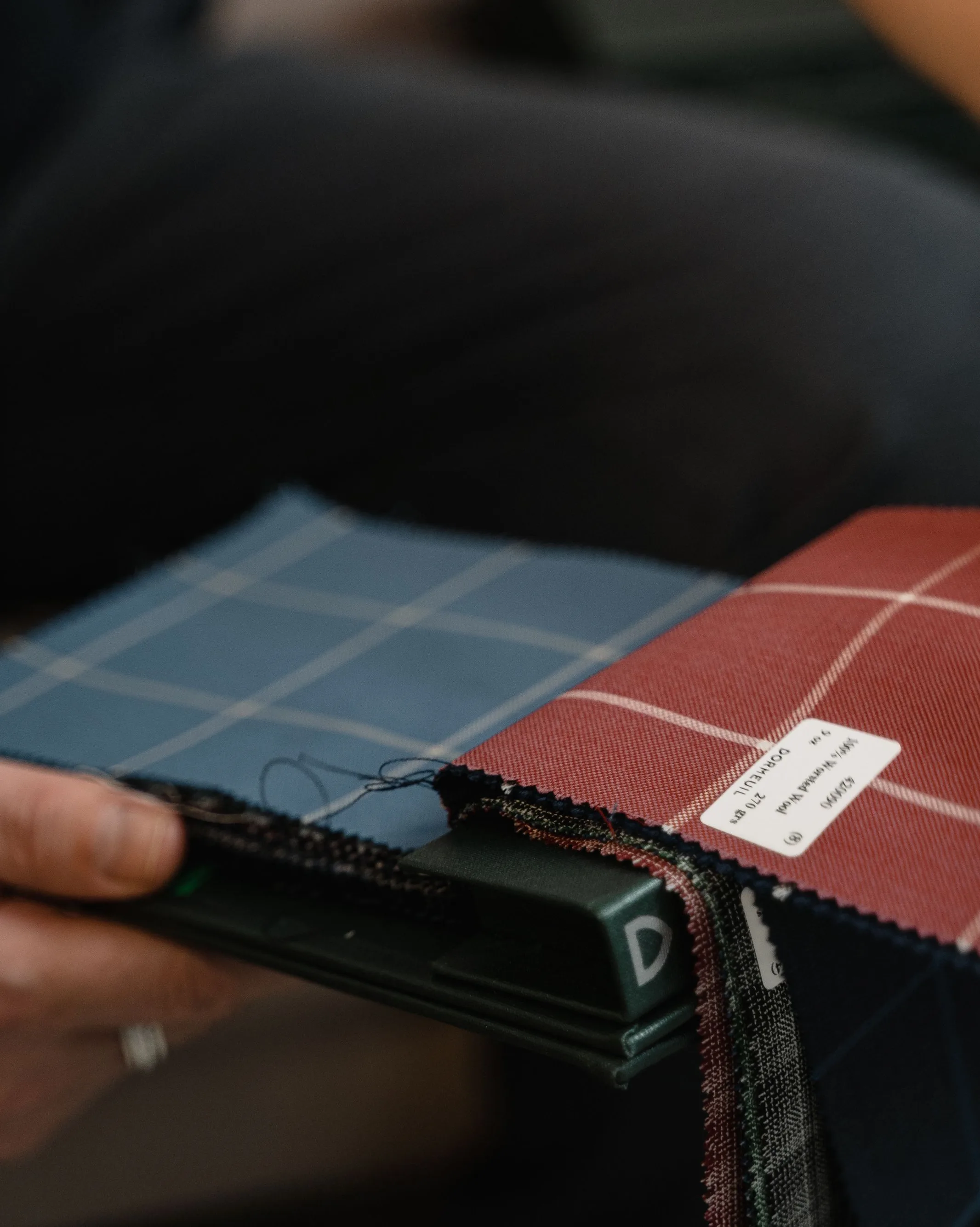 Échantillons de lainage à carreaux et leur étiquette, tenus en main